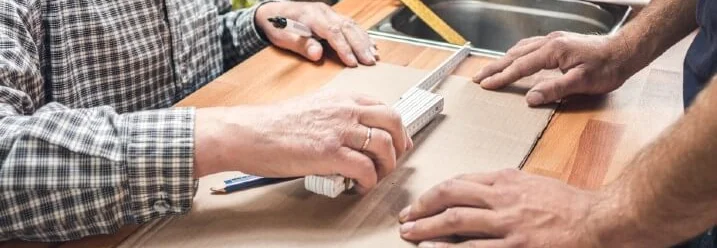 Zwei Personen messen eine Pappe mit einem Zollstock aus
